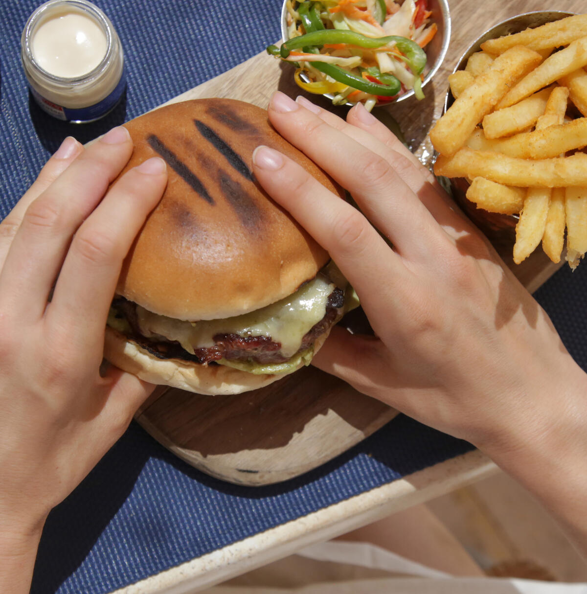 Photo of two hands holding a cheeseburger, one of many high purine foods, with golden fries and peppers on the side.