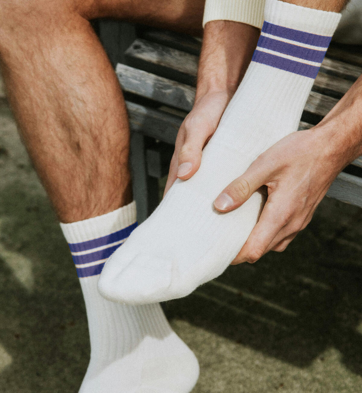 Photo of man wearing white socks with blue stripes, holding his foot due to gout in foot